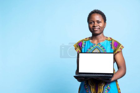 Afrikanisch-amerikanische Person macht Werbung mit weißem Bildschirm auf Laptop und präsentiert drahtlose Computer, die leer isoliert Layout läuft. Junge Frau lächelt in Kamera und hält PC.