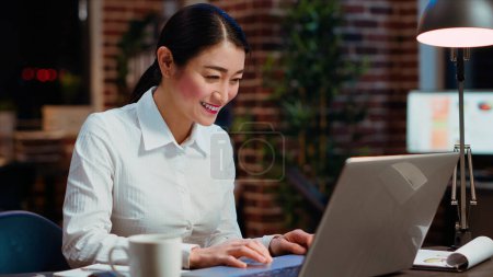 Photo for Asian woman dancing in office, feeling excited after learning of upcoming promotion, rewarded for good results. Cheerful employee singing on computer desk chair, celebrating, camera B - Royalty Free Image