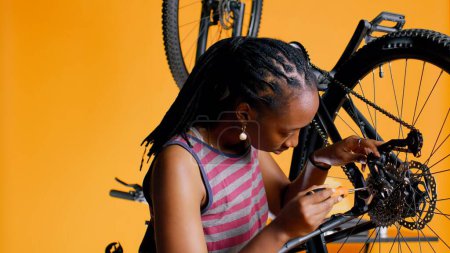 Close up of engineer using screwdriver and hex socket wrench to secure wheel on bicycle in studio background. Professional screwing bolts on bike parts, mending rear derailleur and cassette, camera B