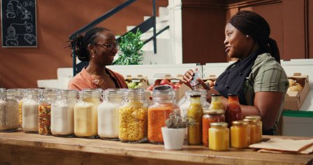 Téléchargez les photos : Vendeur afro-américain donnant échantillon de nourriture au client, présentant de nouvelles collations maison avec des ingrédients naturels. Femme végétalienne essayer des produits du marché avant d'acheter. Coup de main. - en image libre de droit