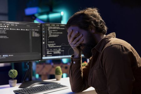 Troubled man facepalming himself while doing software quality assurance, finding major errors in source code. Depressed developer upset after inspecting coding on desktop PC and seeing many issues