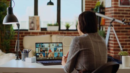 Photo for Remote employee in stylish apartment talking with coworkers during teleconference meeting. Teleworker at home participating in internet videocall with colleagues, camera B - Royalty Free Image