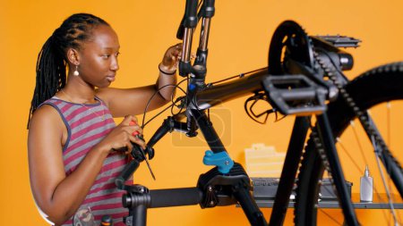 Photo for BIPOC technician uses screwdriver to unmount bicycle handlebars, testing components quality in studio background atelier shop. Specialist mechanic unscrewing bike parts in order to mend them, camera B - Royalty Free Image