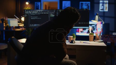 Software developer putting face in hands in frustration while updating binary code script on computer, receiving errors. Admin in apartment exasperated by annoying bugs while programming, camera B