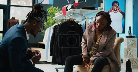Téléchargez les photos : Un employé de magasin afro-américain aide une femme à trouver la bonne pointure de chaussures, une cliente enceinte qui cherche à acheter des chaussures confortables dans un centre commercial local. Client essayant des bottes d'hiver. Caméra B. - en image libre de droit