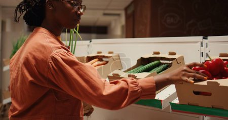 Comprador afroamericano que elige productos orgánicos de cajas, poniendo frutas y verduras en una bolsa de papel para comprar. Mujer comprando productos ecológicos naturales en el mercado de agricultores locales. Cámara 2.