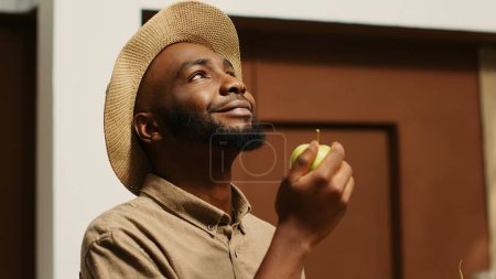 Photo for African american man smelling locally grown apples at supermarket, supporting nonpolluting small business by buying bio food. Client choosing fruits from crates, enjoying natural aroma. Camera 1. - Royalty Free Image