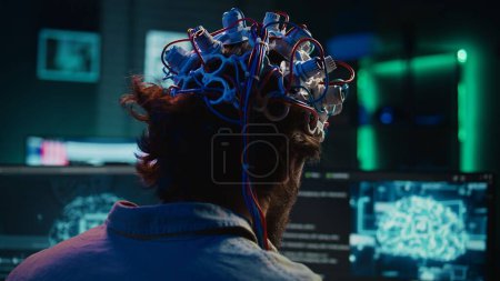 Engineer puts EEG headset on, links brain to cyberspace, conducts experiments. Man merging mind with artificial intelligence, uploading consciousness, achieving superintelligence, camera B close up