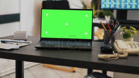 Konzentrieren Sie sich auf den Green-Screen-Laptop auf dem Bürotisch mit einem Computer im verschwommenen Hintergrund, der Börsendaten zeigt. Nahaufnahme eines Notebooks und einer Handelsplattform auf dem PC-Bildschirm im Hintergrund