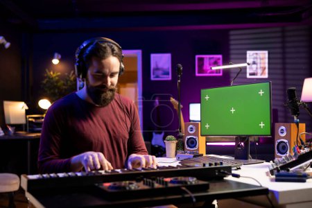 Tontechniker spielt im heimischen Studio elektronische Klaviertastaturen und lernt, Midi-Controller zu spielen, indem er Tutorials auf dem Greenscreen-PC anschaut. Musiker schlägt Synthesizer-Tasten für einen Song.