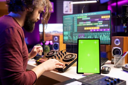 Composer creating soundtracks on stereo gear and greenscreen display on mobile device, mixing and mastering tunes in home studio. Young artist adjusting volume levels on music, daw software.