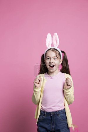 Téléchargez les photos : Fille optimiste excitée agissant étonné par Pâques présente en studio, se sentant heureux avec ses cadeaux et célébrer les vacances de printemps. Petit enfant enthousiaste se réjouissant de la célébration d'avril. - en image libre de droit