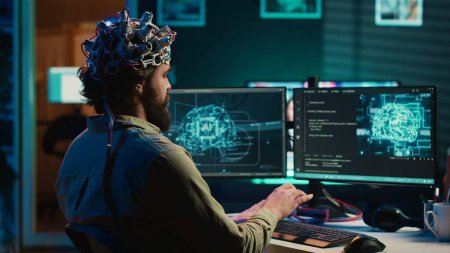 Foto de Hombre con auriculares EEG en el código de escritura que le permite transferir la mente en el mundo virtual de la computadora, convirtiéndose en uno con la IA. Transhumanista usando tecnología neurocientífica para trascender, cámara A - Imagen libre de derechos