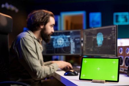Enfócate en el dispositivo de pantalla verde junto al hombre en un fondo borroso actualizando las redes neuronales de inteligencia artificial en el PC. Administrador de TI actualizar la IA de alta tecnología, tableta de maqueta en el escritorio, de cerca