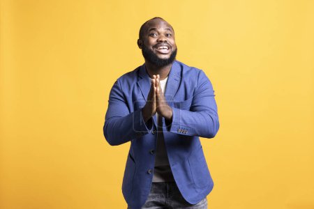 Cheerful african american man putting hands together in appreciation gesture, saying thank you. Happy BIPOC man doing praising gratitude gesturing, isolated over studio background