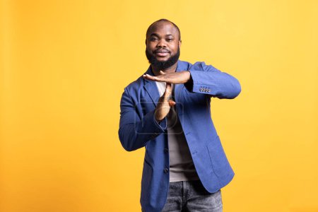 Portrait of smiling african american man asking for timeout, doing hand gestures. BIPOC person doing pause sign gesturing, wishing for break, isolated over studio background
