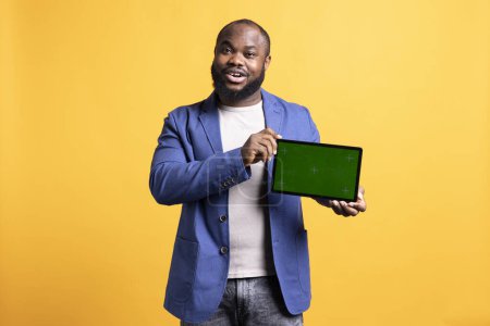 Téléchargez les photos : Homme afro-américain joyeux présentant vidéo sur tablette écran vert en mode paysage, fond de studio. Upbeat BIPOC personne tenant vide espace de copie chroma dispositif clé utilisé pour présenter des annonces - en image libre de droit