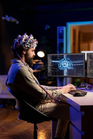 Computeringenieur mit EEG-Headset beim Schreiben von Code, der es ihm ermöglicht, den Geist in die virtuelle Welt zu transferieren und eins mit der KI zu werden. Verrückter Wissenschaftler nutzt neurowissenschaftliche Technologie, um Superintelligenz zu erlangen