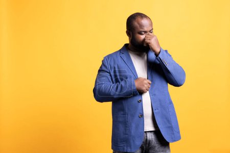 Photo for African american man blowing nose after catching cold during winter, isolated over studio background. BIPOC person suffering from flu, having trouble with sinus infection - Royalty Free Image