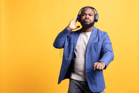 Photo for African american man listening to music on wireless stereo headphones during time off. BIPOC audiophile enjoying songs on high fidelity earphones, isolated over studio background - Royalty Free Image