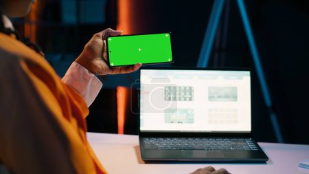 Photo for Business student looks at greenscreen on phone app and learning to use tax service software, money management. Young woman holding device with isolated mockup display, e learning. Camera A. - Royalty Free Image