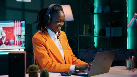 Photo for African american girl jamming on music and writing reports for her final bachelor essay, having fun with songs on headset. Student preparing for exams with class notes and materials. Camera A. - Royalty Free Image