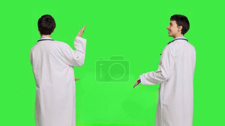 Médecin pointant vers la gauche ou la droite pour créer une publicité sur le Web debout sur fond d'écran vert, faire une publicité marketing en studio. Femme médecin en manteau blanc montre une annonce. Caméra B.
