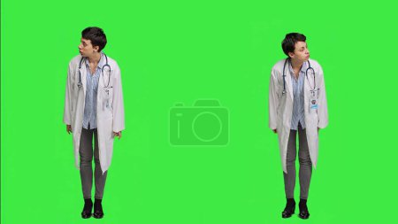 Téléchargez les photos : Femme médecin regardant autour pour les patients à venir à des examens de contrôle, en attendant quelqu'un debout contre fond d'écran vert. Médecin généraliste avec un manteau blanc impatient. Caméra A. - en image libre de droit