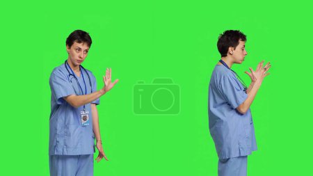 Photo for Displeased irritated nurse shouting no and arguing with someone against greenscreen backdrop, showing rage and anger while she wears hospital scrubs. Aggressive medical assistant. Camera B. - Royalty Free Image