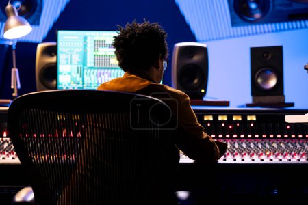 Téléchargez les photos : African American Record Engineer édite et mixe des chansons sur console studio, en utilisant un logiciel numérique sur moniteur pour ajouter des effets audio en post-production. Producteur travaillant sur de la nouvelle musique. - en image libre de droit