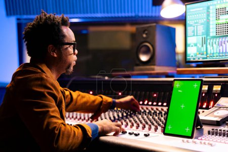 Photo for African american music producer recording and editing tracks in studio, operates panel board next to mockup on device. Sound designer mixing and mastering tunes on audio console, stereo gear. - Royalty Free Image