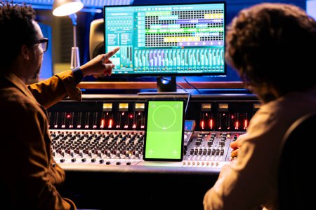 Künstler und Tontechniker arbeiten mit Greenscreen-Displays am Tablet, mischen und Mastering-Tracks mit Audiopult und digitaler Software. Musikerteam, das Musik schneidet, motorisierte Fader.
