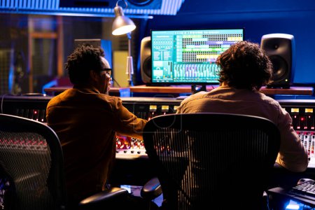 Photo for Professional sound engineer and artist working together on a new track, using digital audio software to edit and process tunes. Experts team collaborating on music, mixing at control room board. - Royalty Free Image