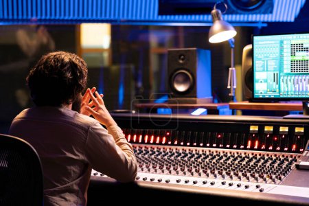 Focused sound designer processing and creating tunes in control room at professional studio, working with digital audio interface. Skilled technician mixing and mastering music, mixer station.