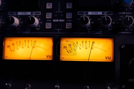 Photo for Technical recording equipment and devices for calibrating volume levels and sound settings in professional studio control room, yellow light. Audio mixer desk with switchers and sliders. Close up. - Royalty Free Image