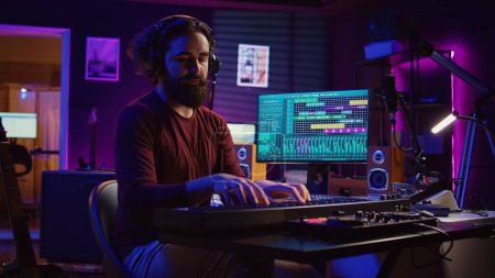 Songwriter-Musiker spielt Gitarre und elektronisches Piano-Keyboard im Heimstudio, nimmt Akustik mit Monitoren auf, um neue moderne Songs zu produzieren. Equalizer und Daw-Software. Kamera B.