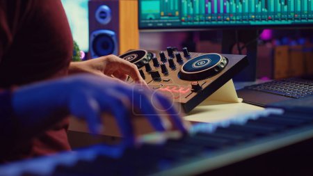 Photo for Skilled artist playing piano keyboard and recording sounds on daw software, capturing audio track instruments and vocals. Producer creating songs with mixing console in post production. Camera A. - Royalty Free Image