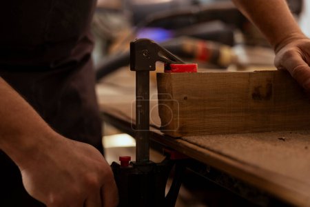 Téléchargez les photos : Charpentier utilisant l'étau de banc pour tenir bloc de bois, début de l'assemblage de meubles en atelier, gros plan. Fabricant en menuiserie à l'aide de l'outil vice pour saisir un morceau de bois avant de le sculpter - en image libre de droit