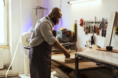 Photo for Craftsperson at workbench selecting high quality wood materials for commissioned project. African american woodworking professional doing quality assurance on timber piece - Royalty Free Image