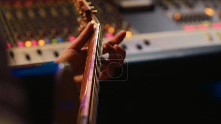 Téléchargez les photos : Chanteur musicien enregistrant une nouvelle chanson sur sa guitare électro acoustique, créant une nouvelle musique dans la salle de contrôle du studio professionnel. Artiste jouant en direct avec un instrument. Ferme là. Caméra A. - en image libre de droit