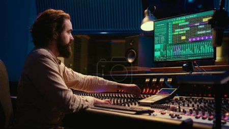Photo for Professional tracking engineer editing music by adding sound effects in control room at studio, recording tracks and using mixing console. Producer operates technical equipment. Camera B. - Royalty Free Image