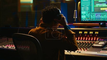 Photo for African american sound designer removing tonal imbalances and white noise on recorded files, music industry post production in professional studio. Control room expert editing tracks. Camera A. - Royalty Free Image