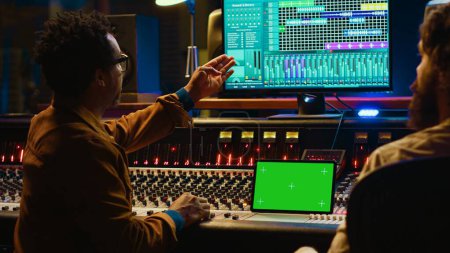 Professioneller Ingenieur und Musiker mischt Tracks neben isolierten Displays auf dem Tablet und bearbeitet Audio nach der Aufnahmesession, um einen Hit zu produzieren. Künstler arbeitet mit Sounddesigner zusammen. Kamera A.