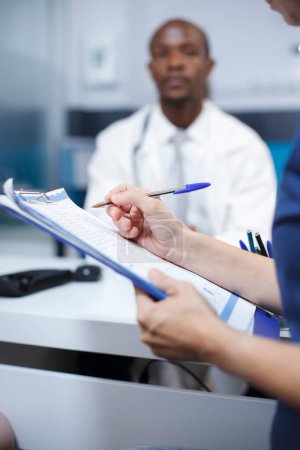 Gros plan d'une patiente remplissant des documents pour son examen médical avec le médecin de l'hôpital. Des soins de santé et des conseils de qualité sont fournis dans cette consultation.