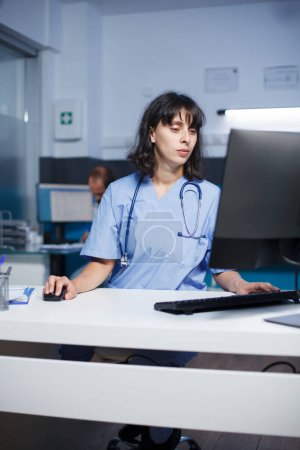 In der Praxis analysieren engagierte Ärzte mit Hilfe von Computern Patientenakten. Krankenschwester überprüft Patientendaten auf einem Desktop-Computer im Krankenhaus mit konzentrierter Aufmerksamkeit.