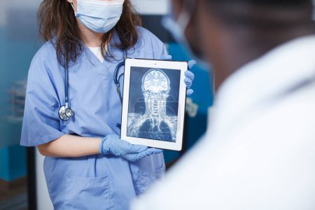 Photo for Doctor analyzes medical results for patients in an office. Examining the findings using a digital tablet and a screen displaying a skull scan. Scene conveys professionalism and expertise in neurology. - Royalty Free Image