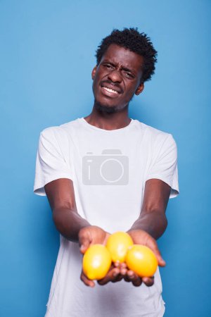 Photo for African american person holding lemons for healthy vegetarian diet. Man presenting yellow citrus fruits in hands for natural nutrition with vitamins. Adult showing fresh juicy fruits to camera. - Royalty Free Image