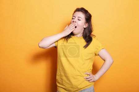 Photo for Portrait of caucasian woman yawning and covering her mouth, feeling sleepy in studio. Tired female person falling asleep while posing and standing over isolated background. - Royalty Free Image