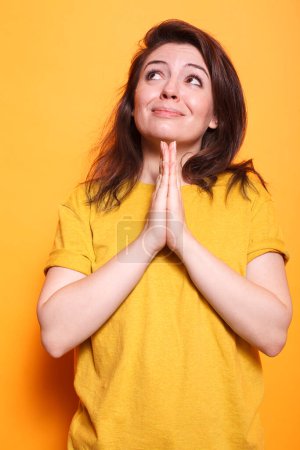 Casual caucasian lady hopelessly looking up and praying with palms close together in front of isolated background. Humble young woman being religious having hope and faith.