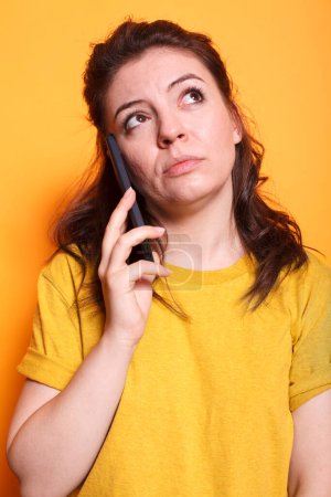 Photo for Portrait of female individual having important phone call conversation in front of isolated background. Close-up of woman in thoughts while talking on her mobile device with friends and family. - Royalty Free Image